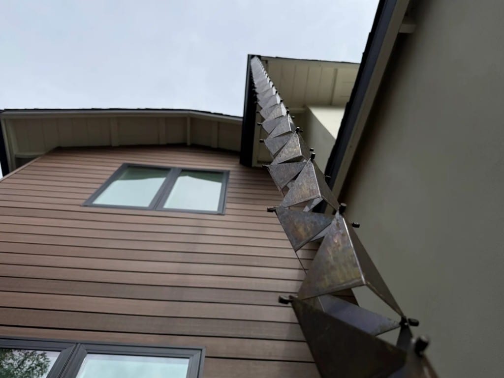 Decorative rain chain hanging from a dark gutter