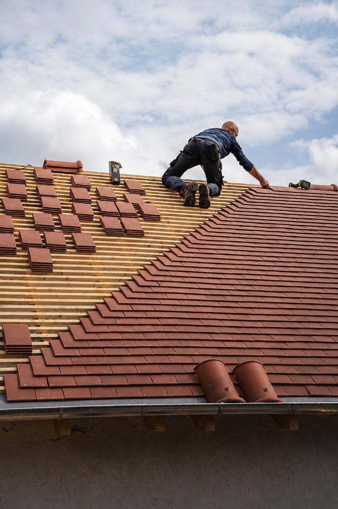 Roofer installing flat clay tiles on wooden battens